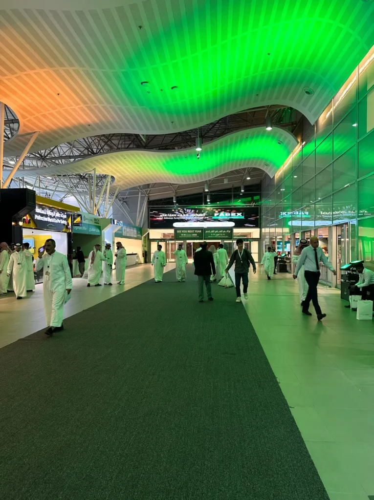 Visitors walking through the FABEX Saudi Arabia exhibition hall under green lighting.