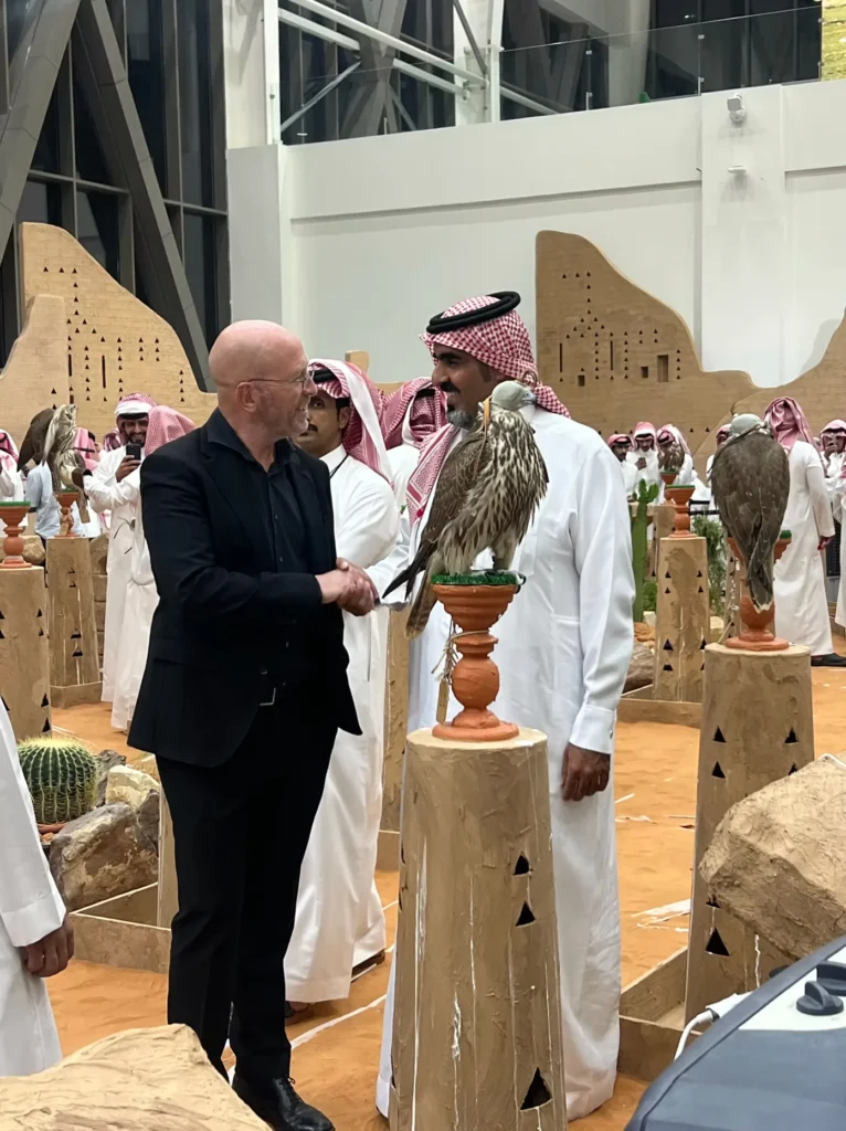 International visitor greeting a Saudi falconer beside a falcon at the exhibition.