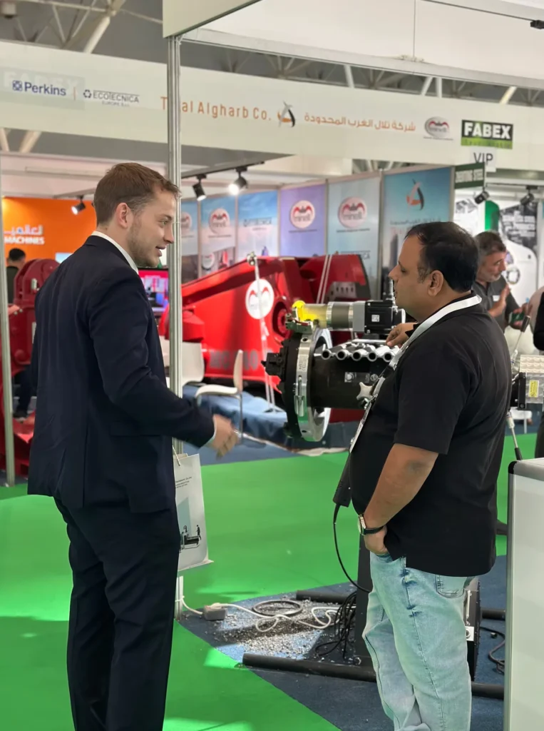 Business discussion beside industrial machinery at the FABEX Saudi Arabia exhibition.
