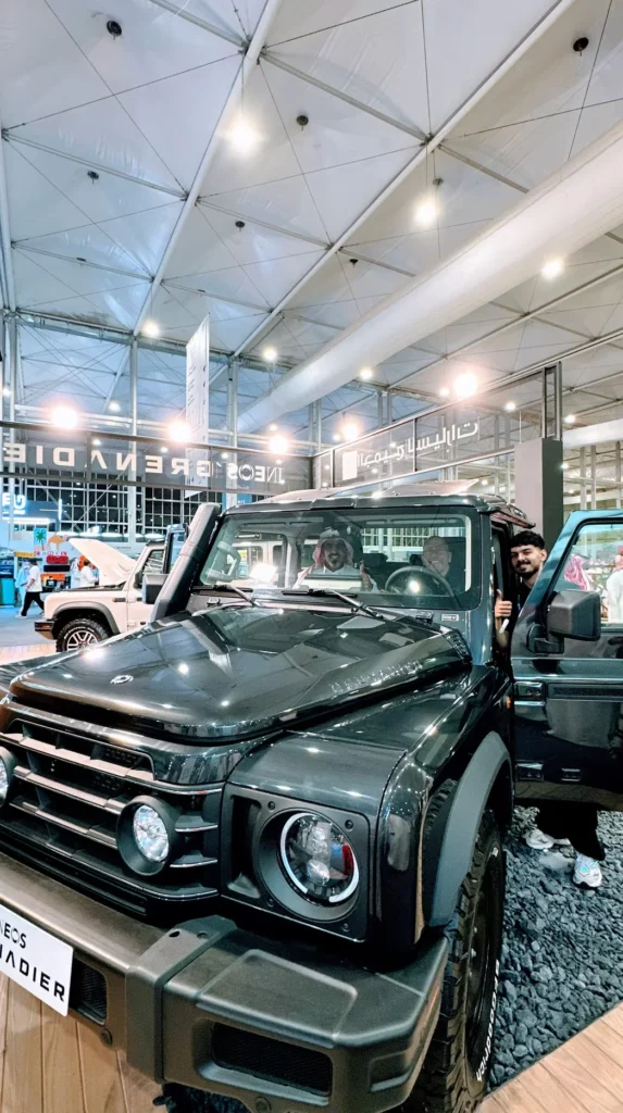 Visitors exploring a dark green Ineos Grenadier off-road vehicle at the exhibition.