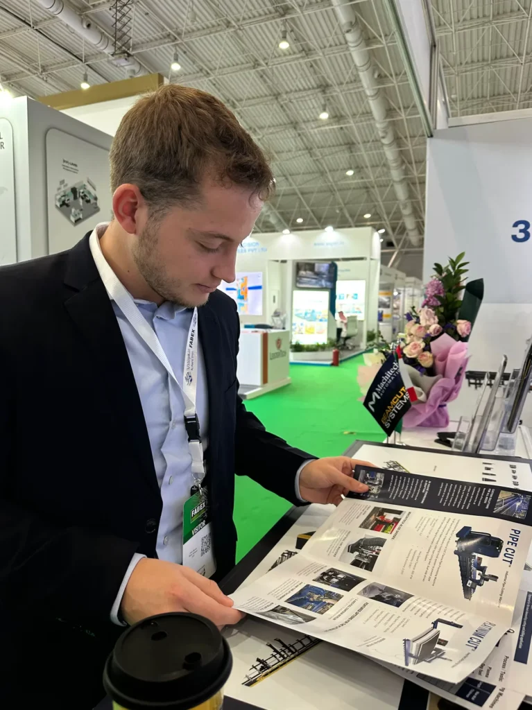 Visitor reviewing an industrial pipe cutting machinery brochure at FABEX Saudi Arabia.